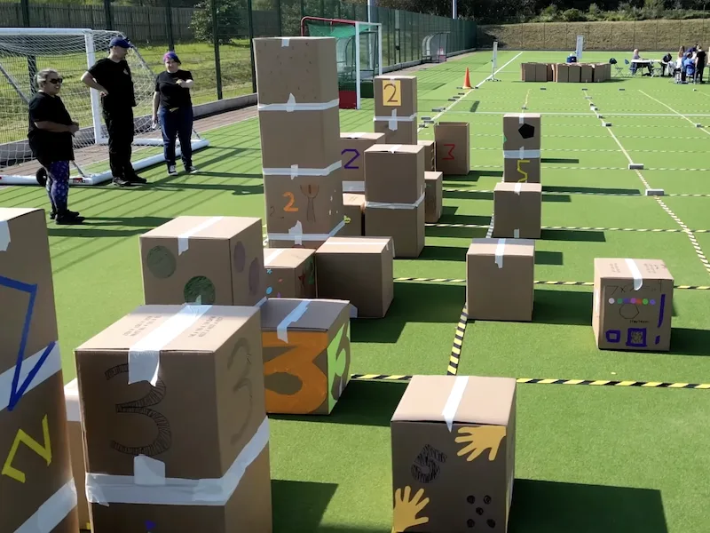 Photo of the Number City project, showing a city made from cardboard boxes; Matt and Katie (and Hana) are standing off to hte left
