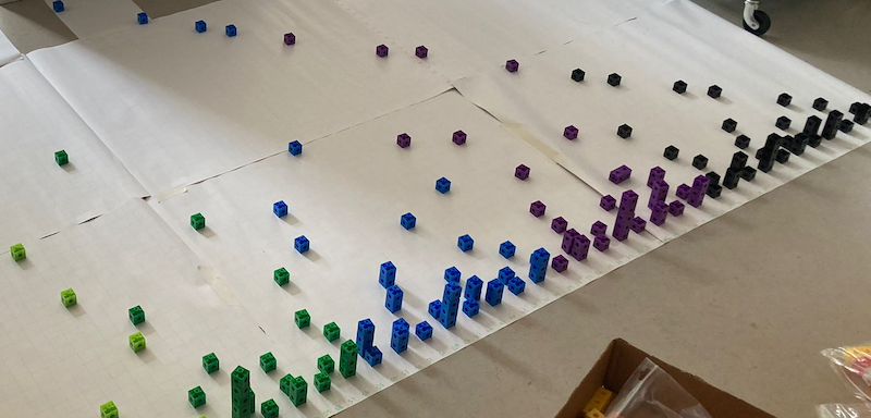 Photo of a mini-Number City built on a large sheet of paper on the floor using Multilink cubes