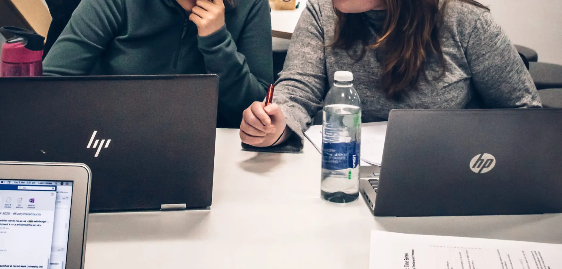 Photo of two people sitting behind laptops at a desk, thinking about a mathematical question